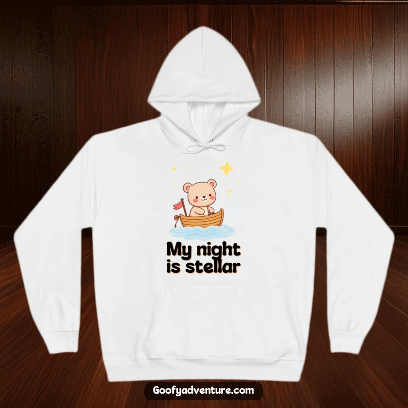 Funny hoodie depicting a happy bear sailing a small boat across a glistening ocean beneath a vast, star-filled night sky.